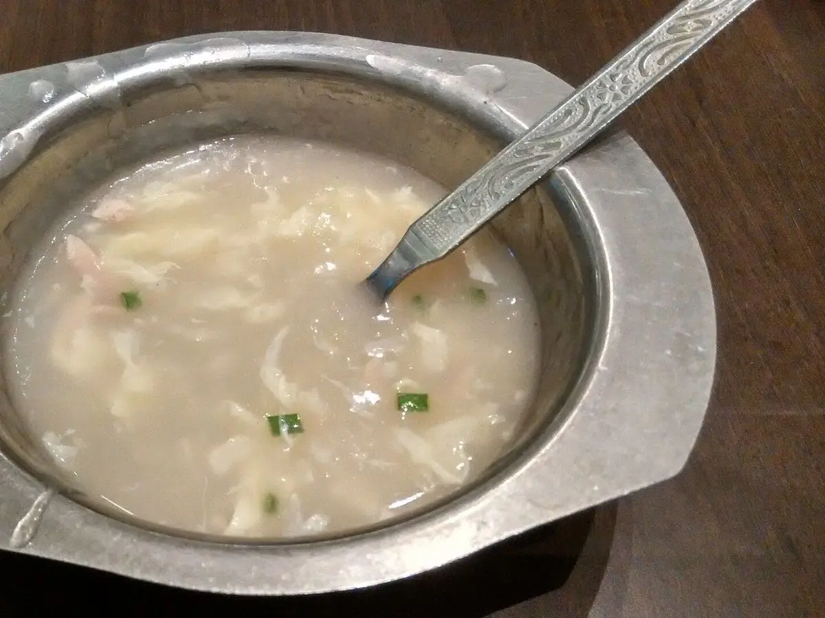 Cuenco metálico de sopa cremosa con hilos de huevo y cebollino picado