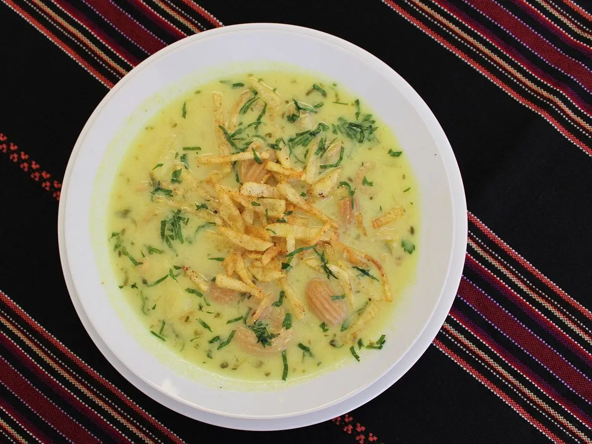 Plato de sopa cremosa de cacahuete con patatas fritas finas y perejil sobre un mantel de rayas