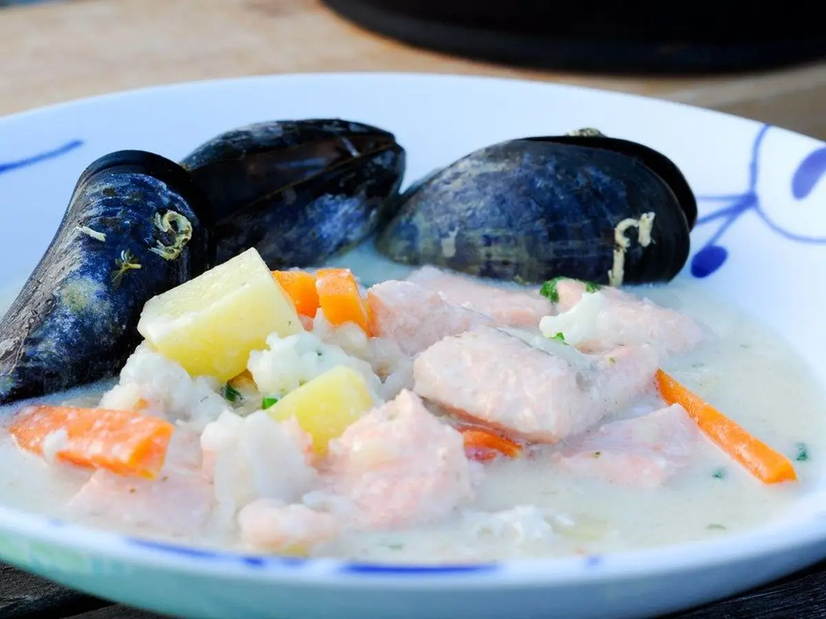 Plato hondo de sopa cremosa de pescado con patata, zanahoria y mejillones en su concha