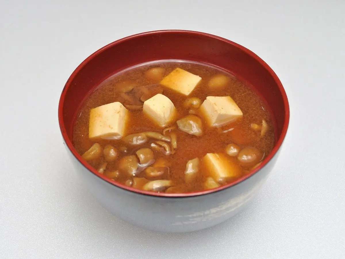 Cuenco rojo de sopa de miso con cubos de tofu y setas sobre un fondo blanco