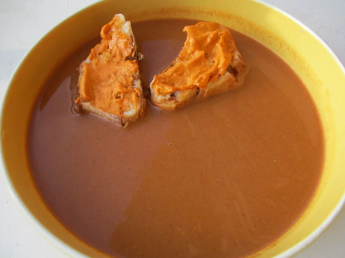Plato hondo de sopa de pescado de roca triturada, color teja, con dos picatostes untados de salsa rouille