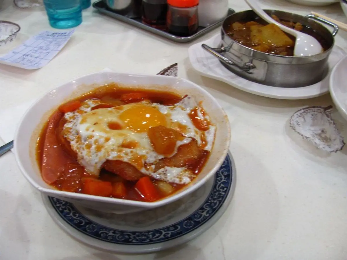 Cuenco blanco con sopa de tomate, huevo y trozos de embutido sobre un plato decorado