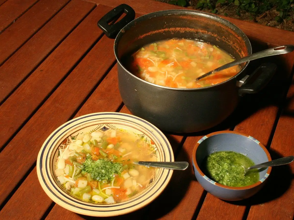 Olla negra y plato hondo de sopa de verduras y alubias con salsa pistou sobre mesa de madera