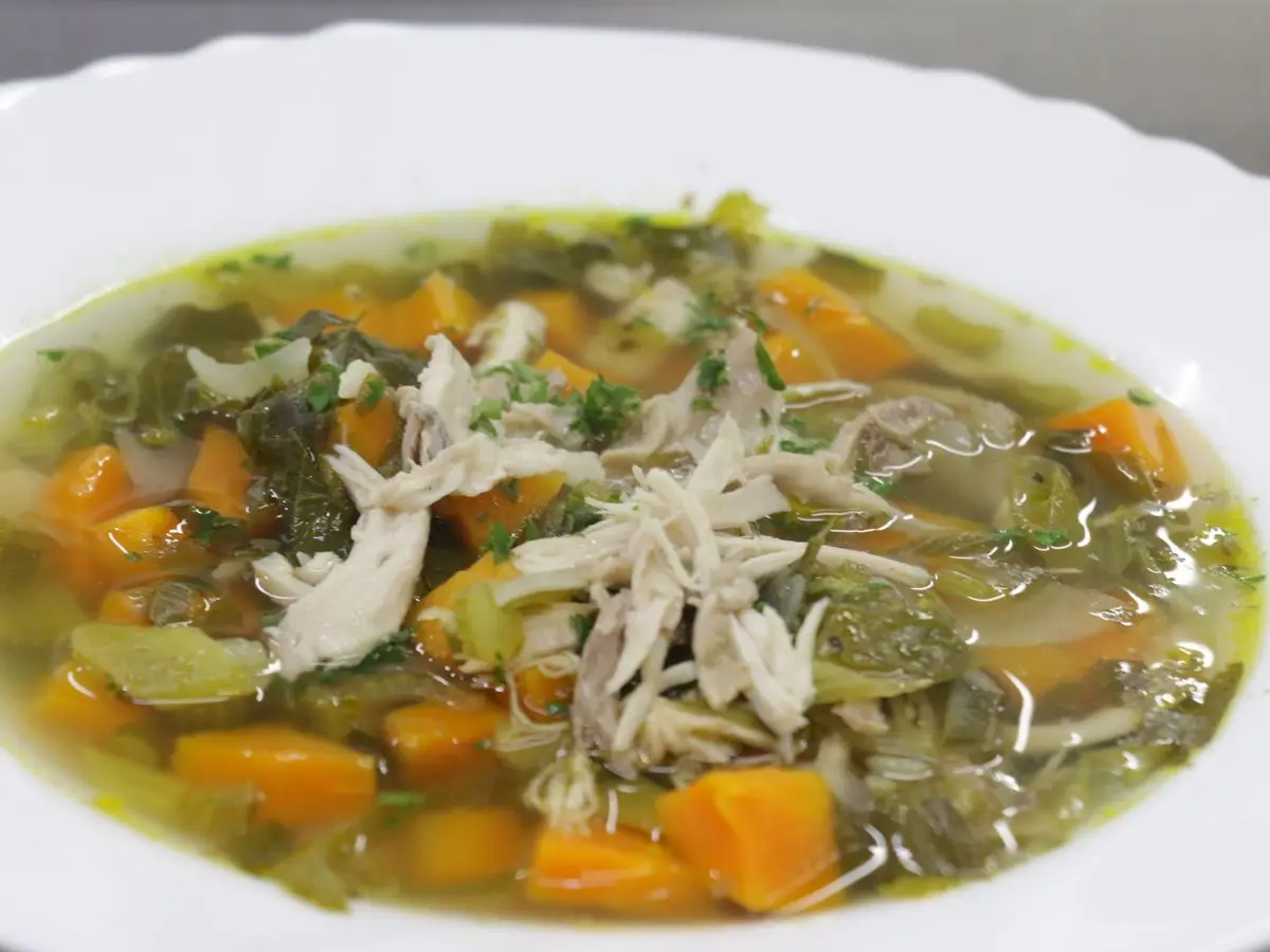 Sopa de caldo claro con pollo desmenuzado, zanahoria y verduras en un plato hondo blanco