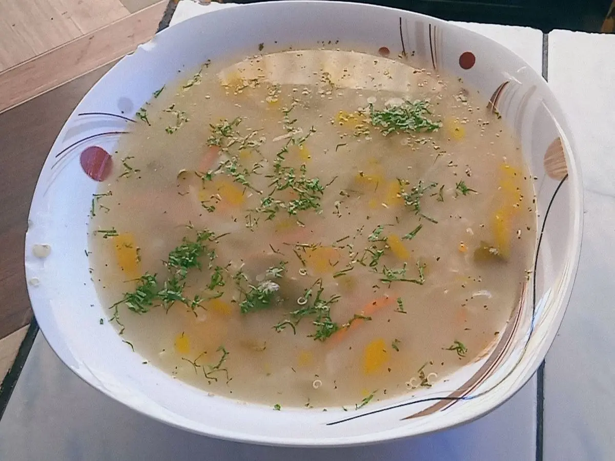 Plato hondo de sopa de quinua con verduras en dados y hierbas picadas