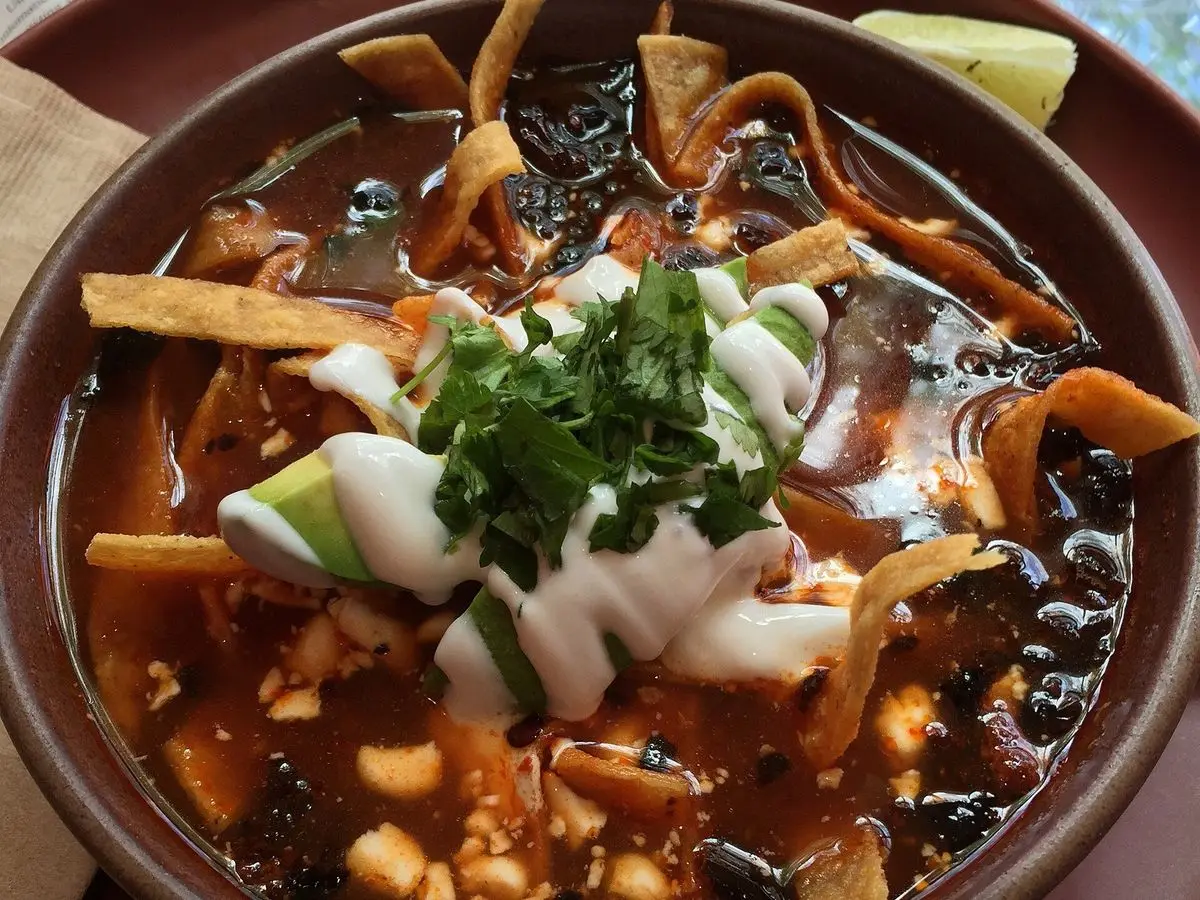 Cuenco de sopa de tortilla con tiras de tortilla, queso, crema, aguacate y cilantro