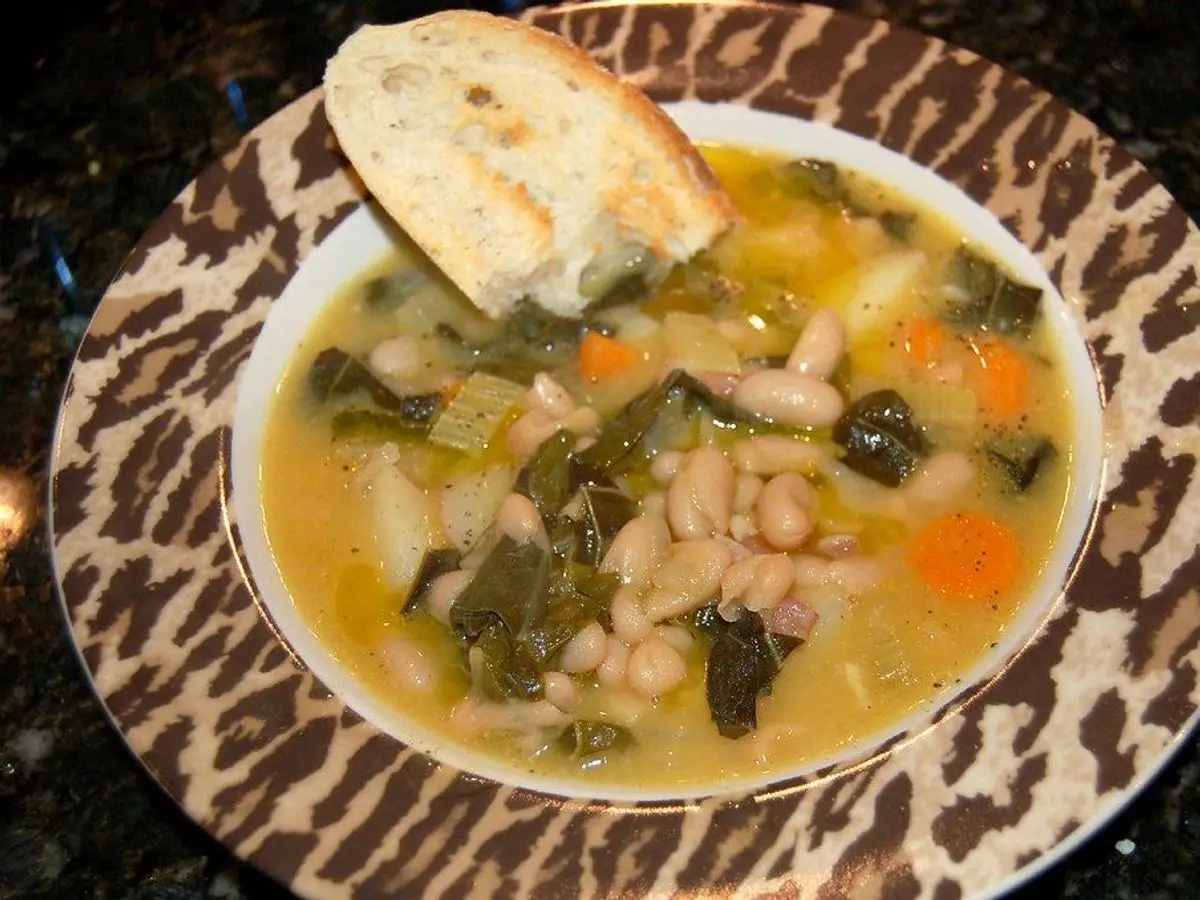 Plato hondo de sopa de alubias blancas con col rizada y zanahoria, con una rebanada de pan
