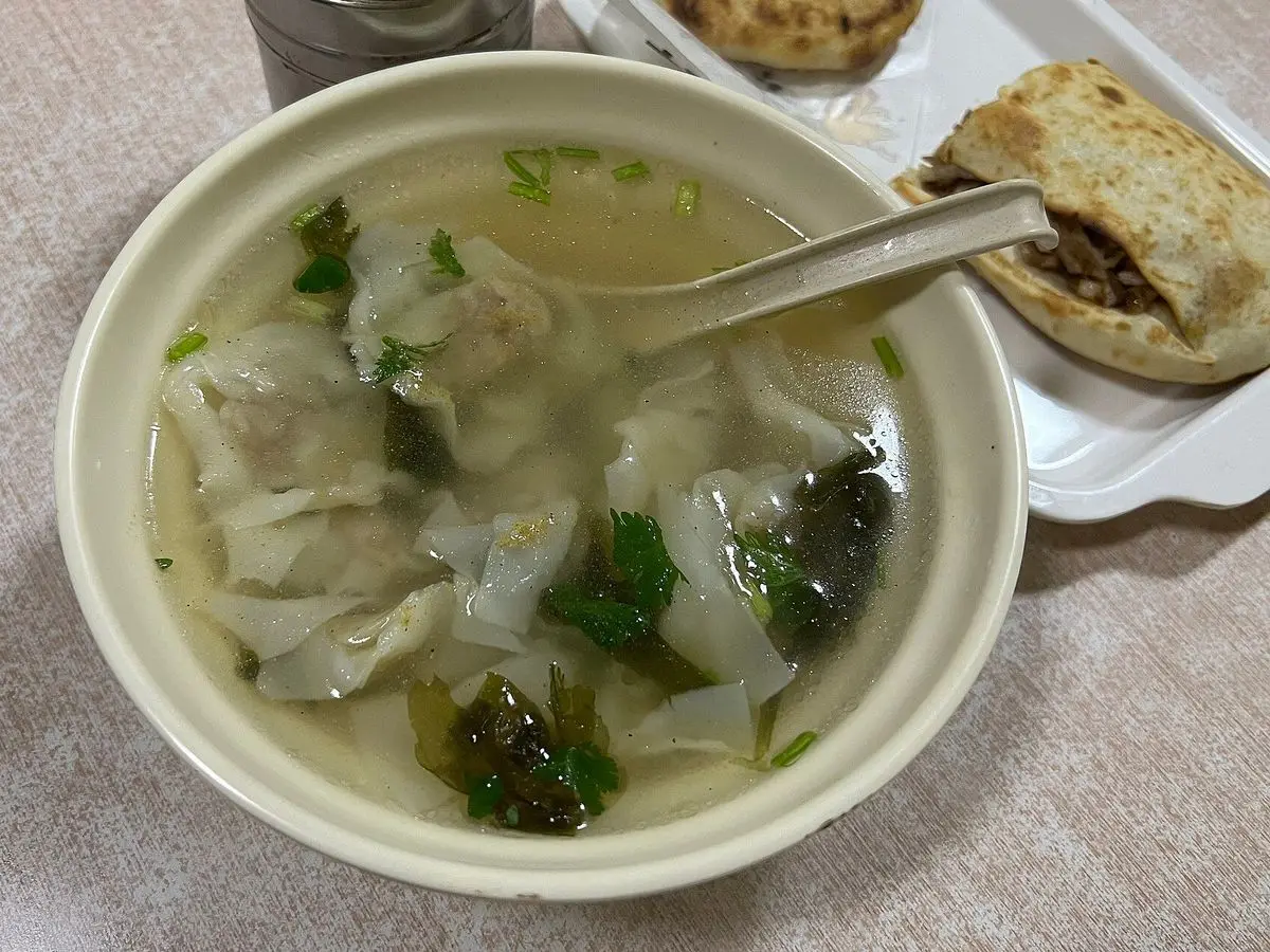Cuenco de sopa de wontons con caldo claro y verduras verdes sobre una mesa