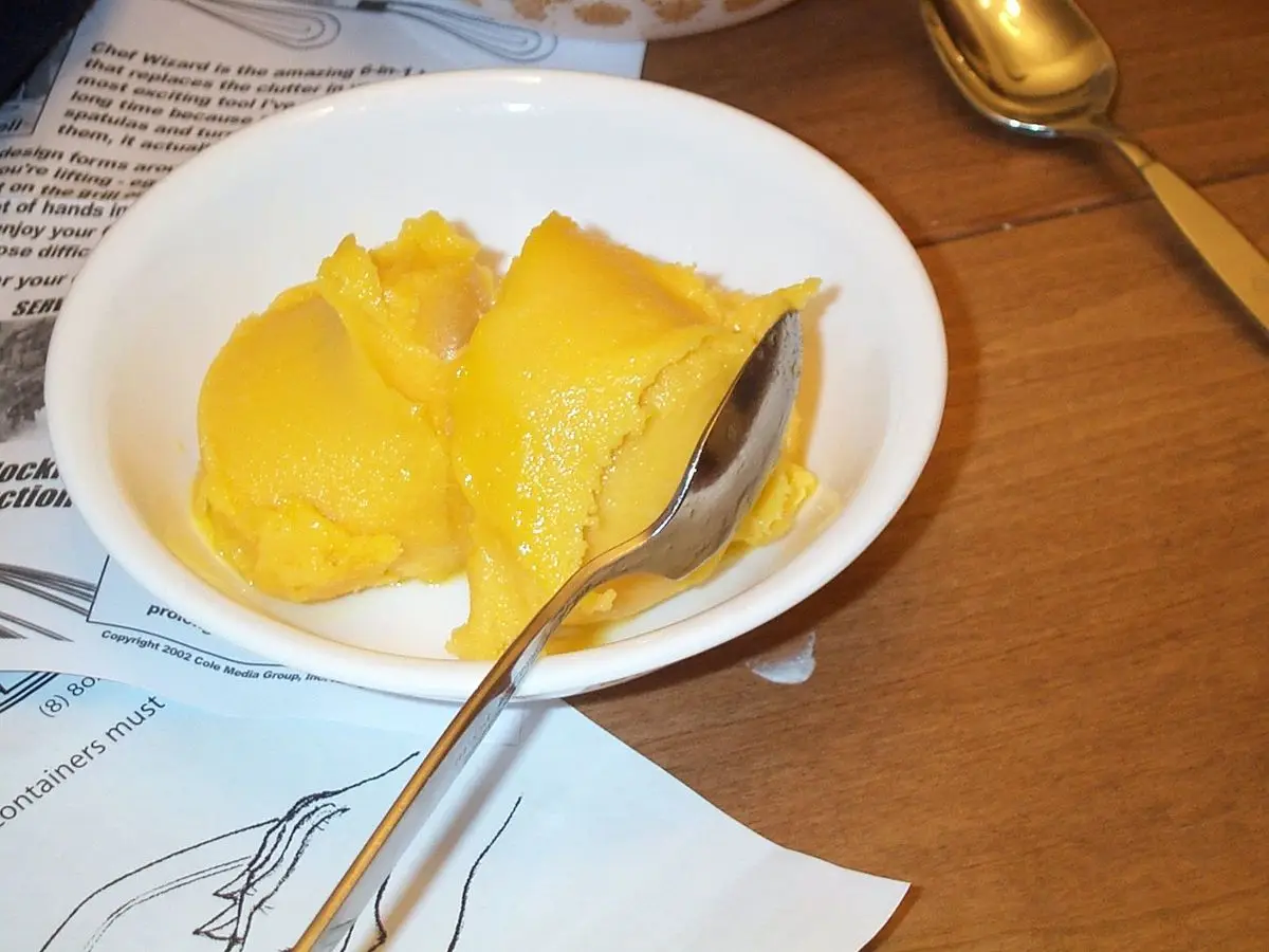 Cuenco blanco con bolas de sorbete de mango amarillo y una cuchara