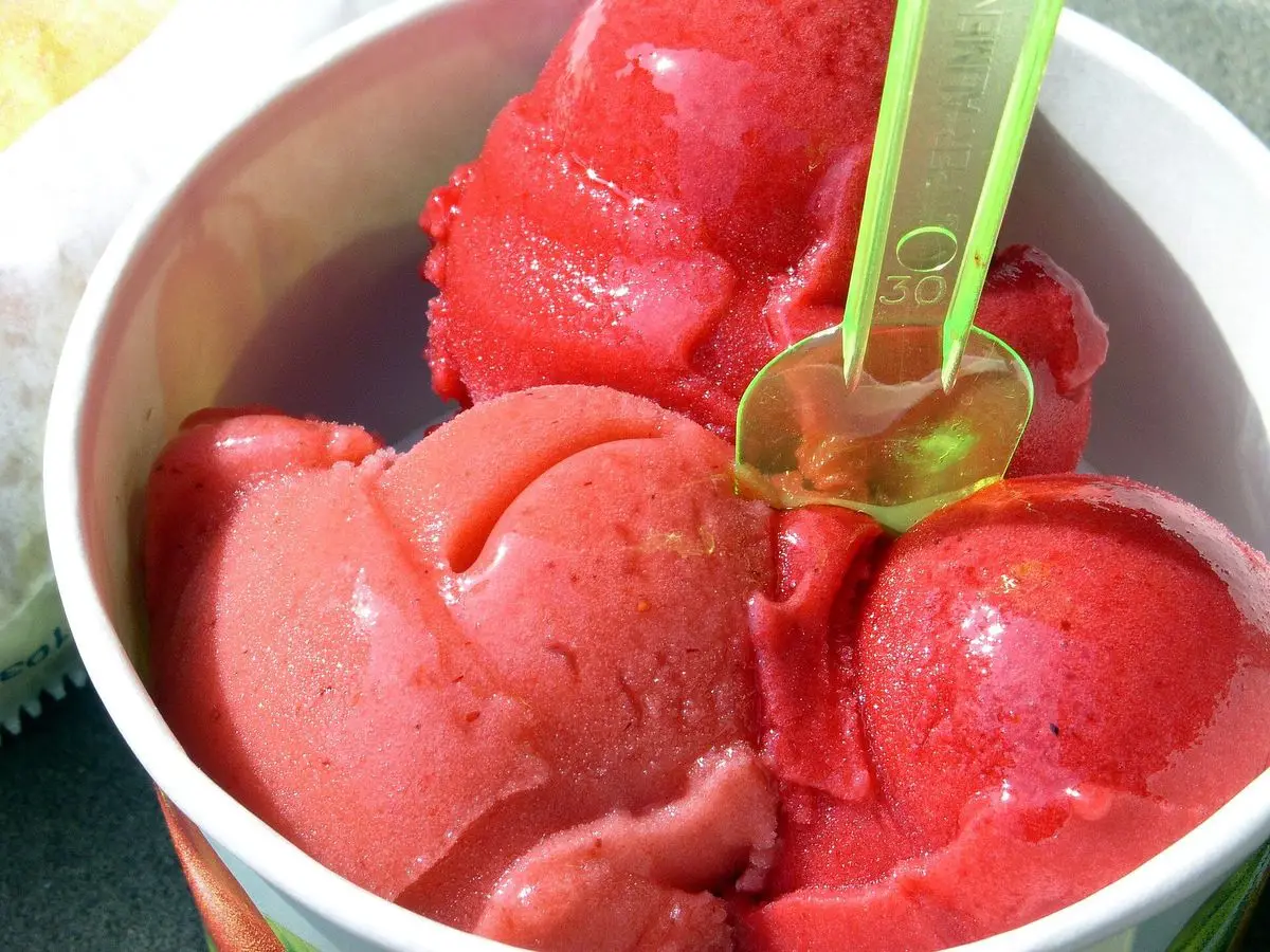 Vasito con bolas de sorbete rosa rojizo de fruta y una cucharita verde