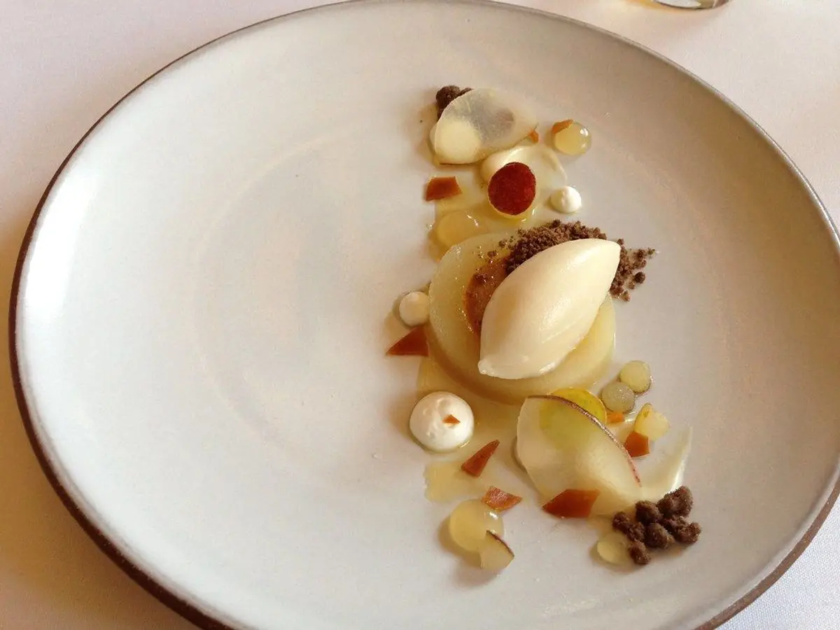 Plato blanco con una quenelle de sorbete de pera y trocitos de pera escalfada alrededor