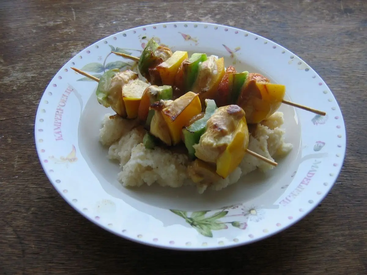 Brocheta de carne con pimiento verde, cebolla y albaricoque sobre una base blanda en un plato blanco