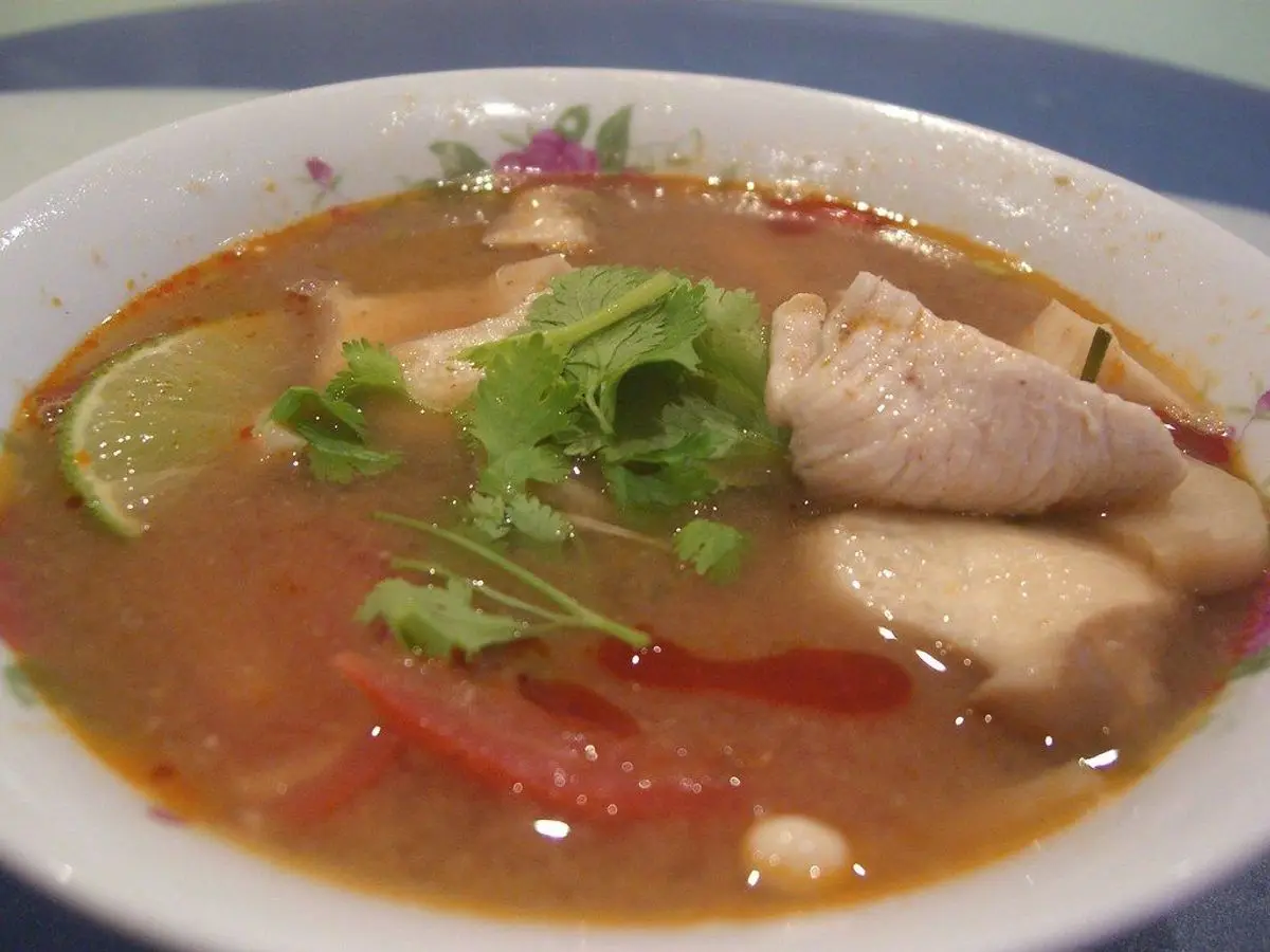 Cuenco de caldo de pollo con trozos de pollo, un gajo de lima, cilantro fresco y tomate