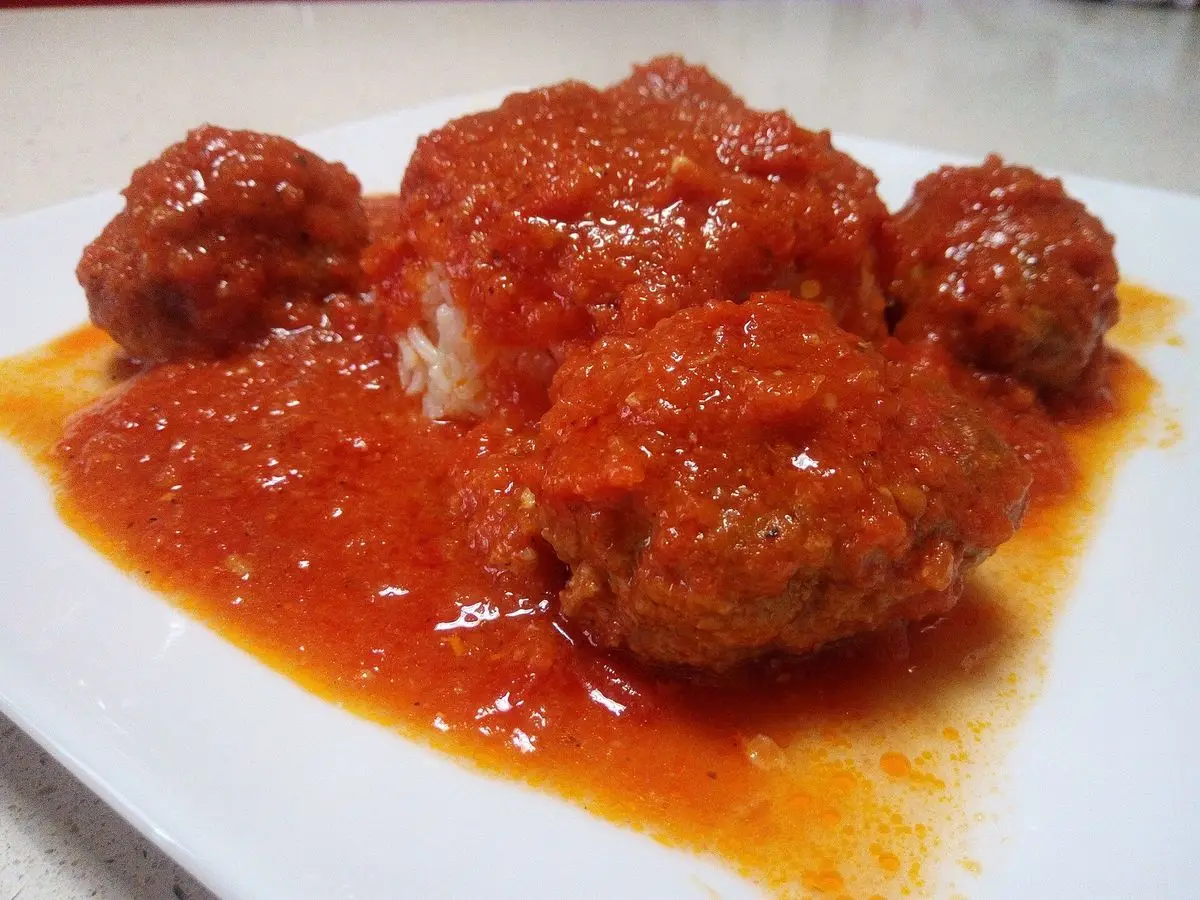 Albóndigas alargadas de carne cubiertas de salsa de tomate sobre un plato blanco