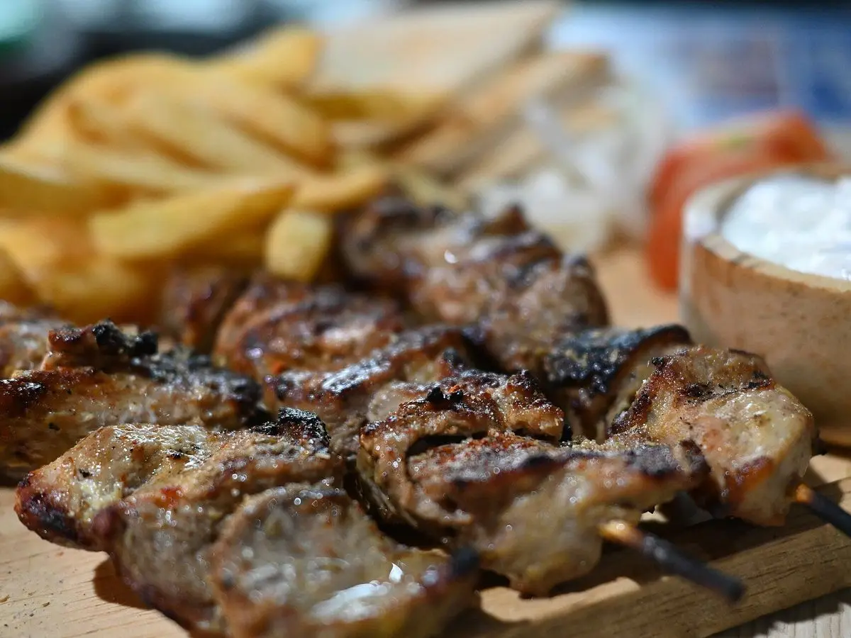 Brochetas de cerdo a la parrilla con patatas fritas y un cuenco de salsa de yogur