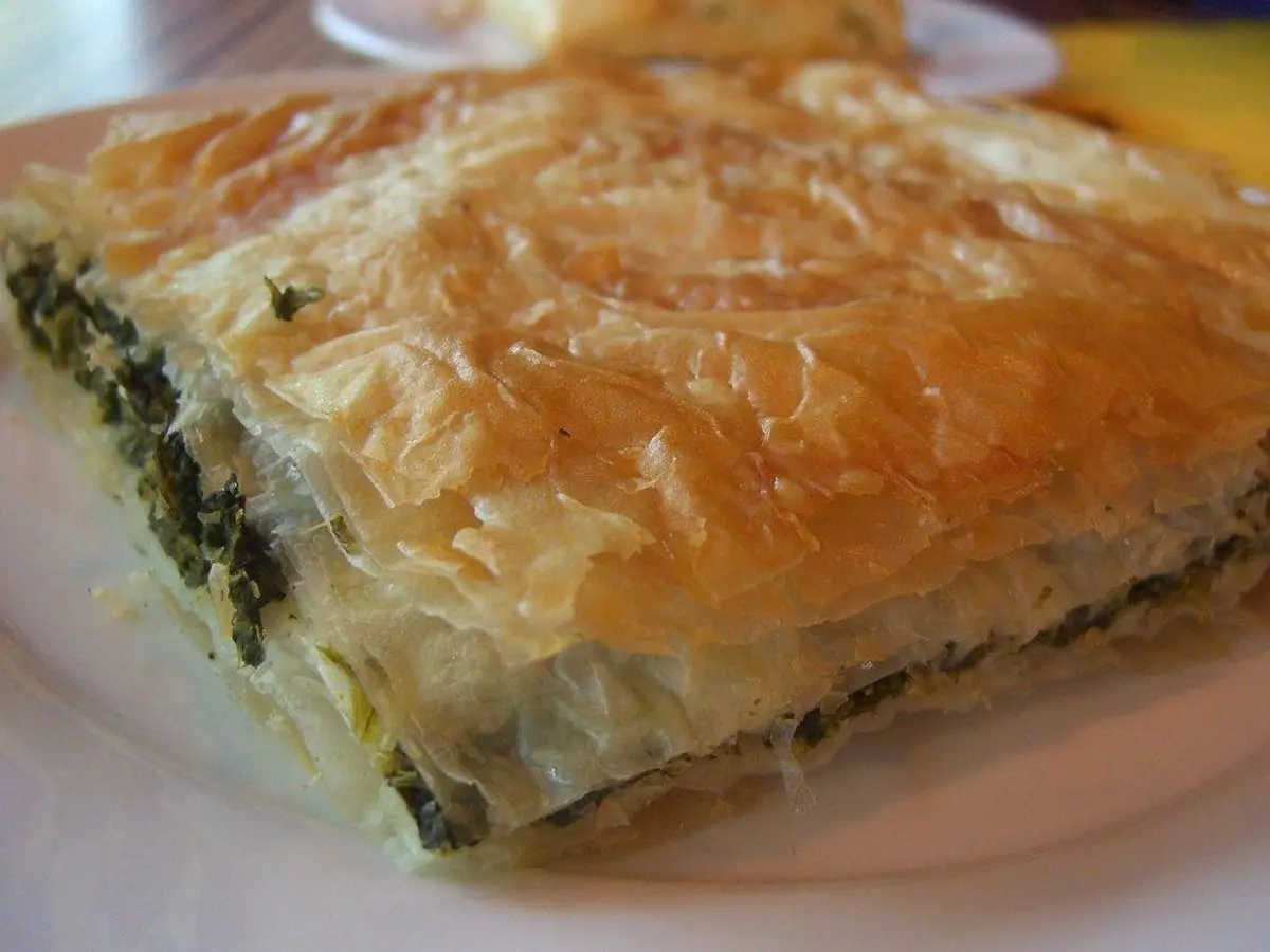 Porción de pastel de hojaldre filo relleno de espinacas en un plato blanco