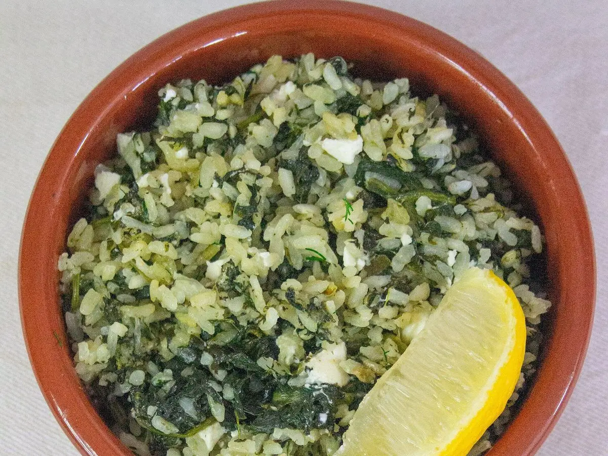 Cuenco de barro con arroz con espinacas, trocitos de feta y una cuña de limón