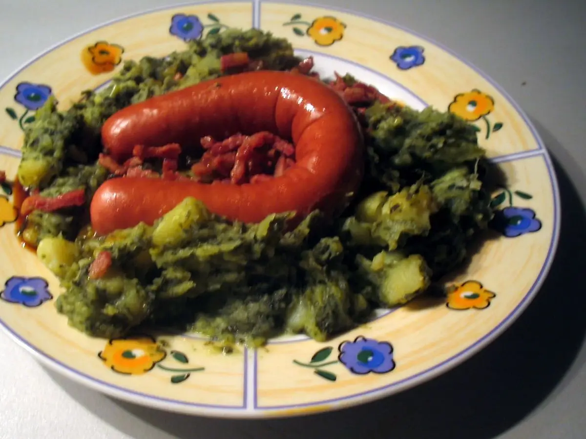 Plato de col rizada con patata aplastada y una salchicha enrollada