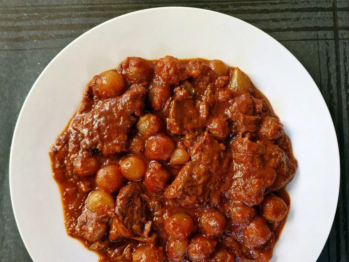 Guiso de ternera con cebollitas en salsa de tomate rojiza servido en un plato blanco