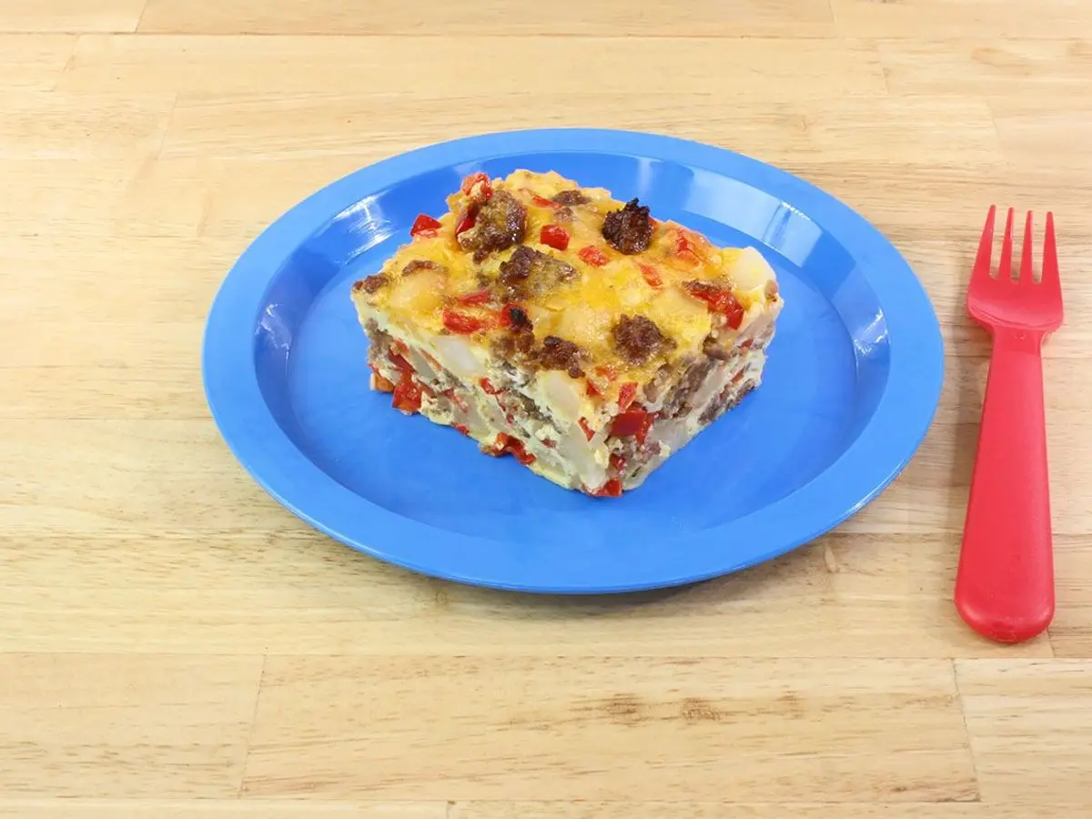 Porción de plato horneado de huevo y pan con verduras en un plato azul con un tenedor