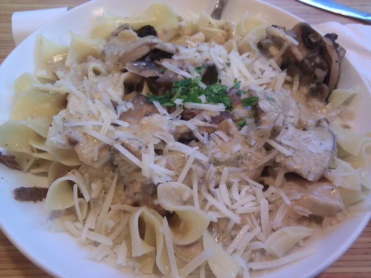Plato de tallarines con salsa cremosa de champiñones, queso rallado y perejil, al estilo stroganoff