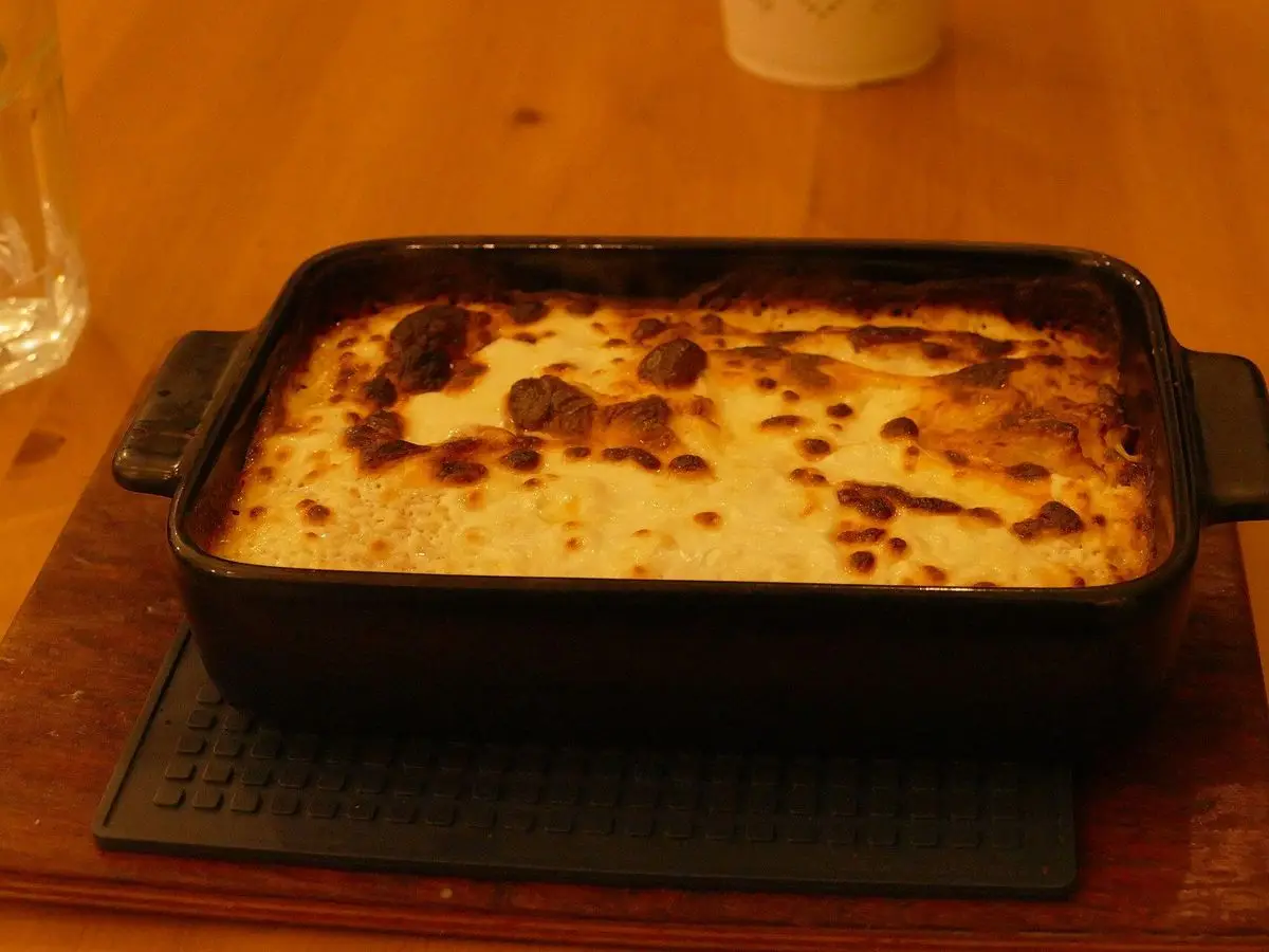 Fuente negra con štrukli horneados, masa rellena de requesón gratinada y dorada, sobre una tabla de madera