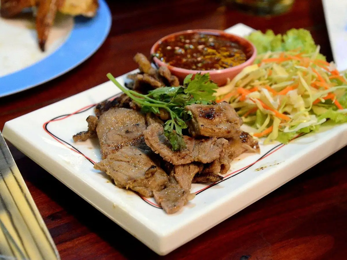 Lonchas de ternera a la brasa con salsa picante jaew, ensalada de col y zanahoria en una bandeja blanca