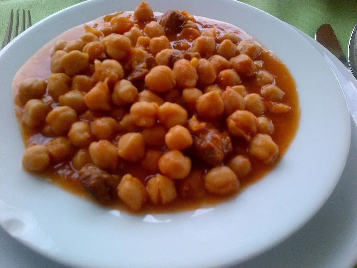 Plato blanco de garbanzos guisados con trozos de ternera en salsa de tomate anaranjada