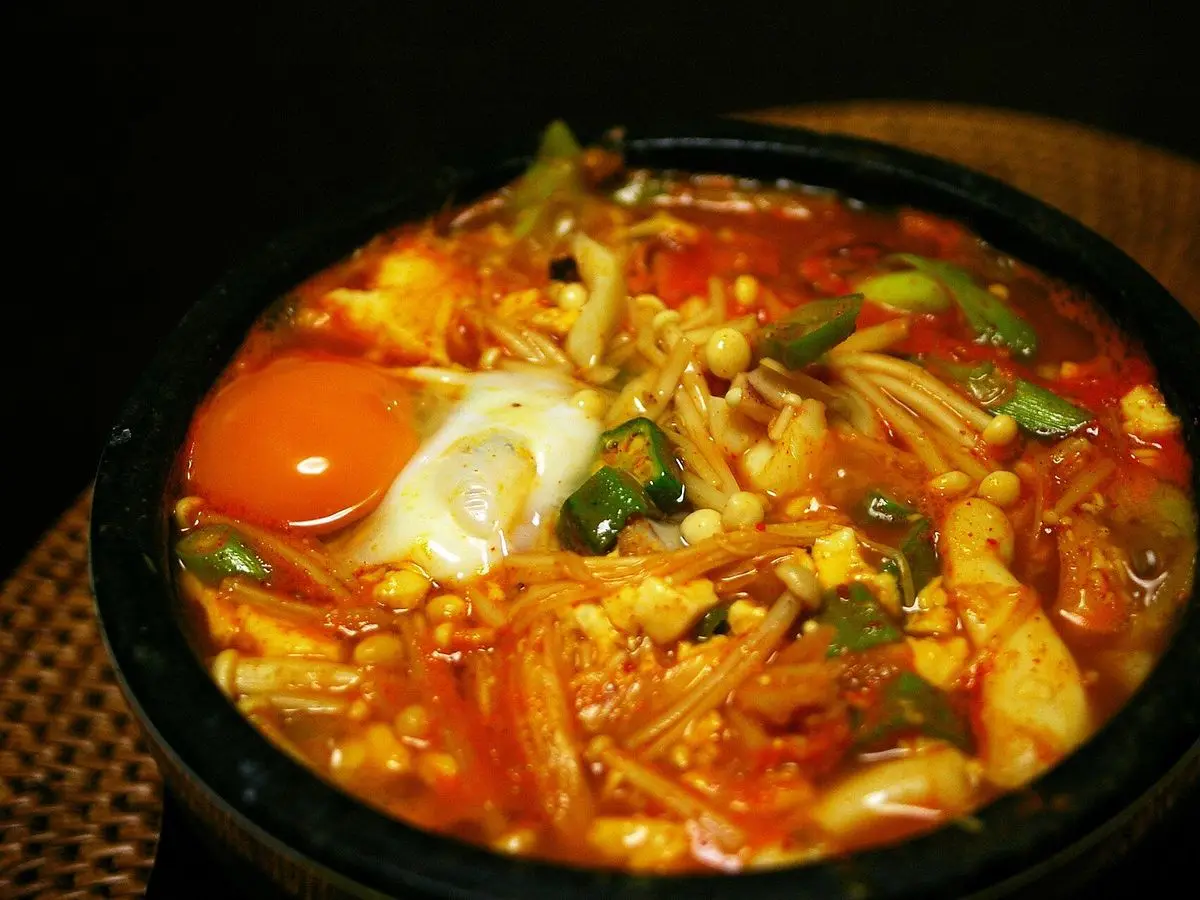 Cuenco de piedra con guiso coreano picante de tofu sedoso, setas enoki y un huevo