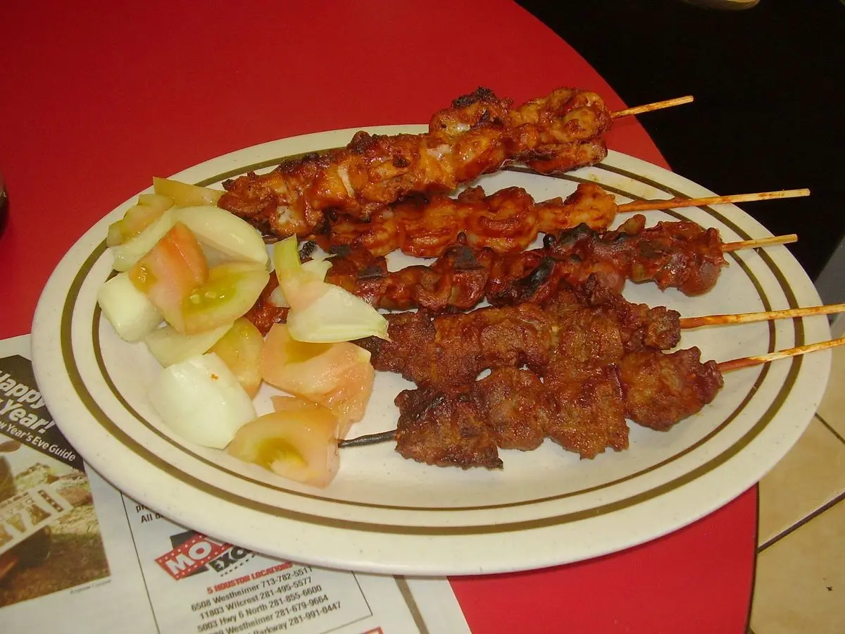 Brochetas de carne especiadas en un plato con cebolla y tomate en rodajas