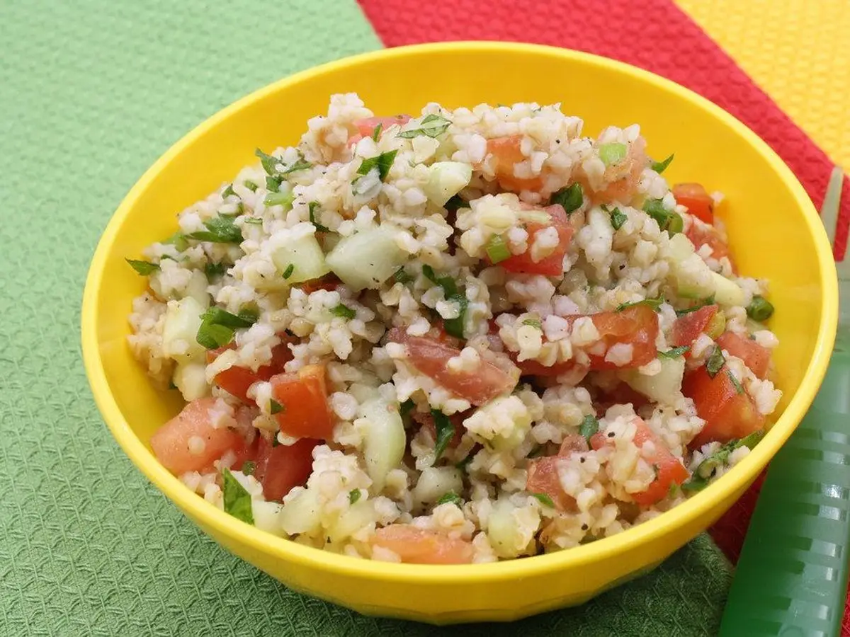 Tabulé de bulgur con tomate, pepino y perejil picados en un cuenco amarillo