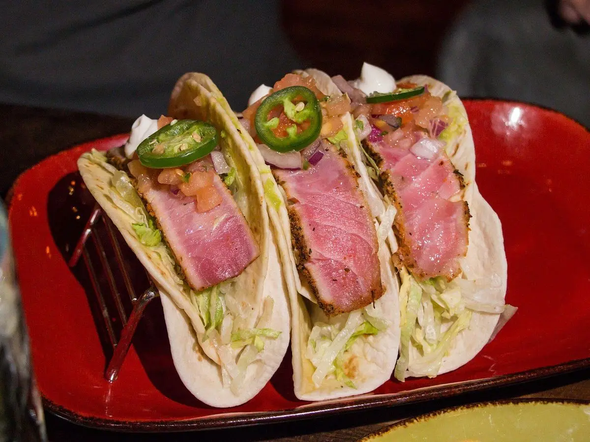 Tres tacos de atún sellado en lonchas con rodajas de jalapeño sobre una bandeja roja