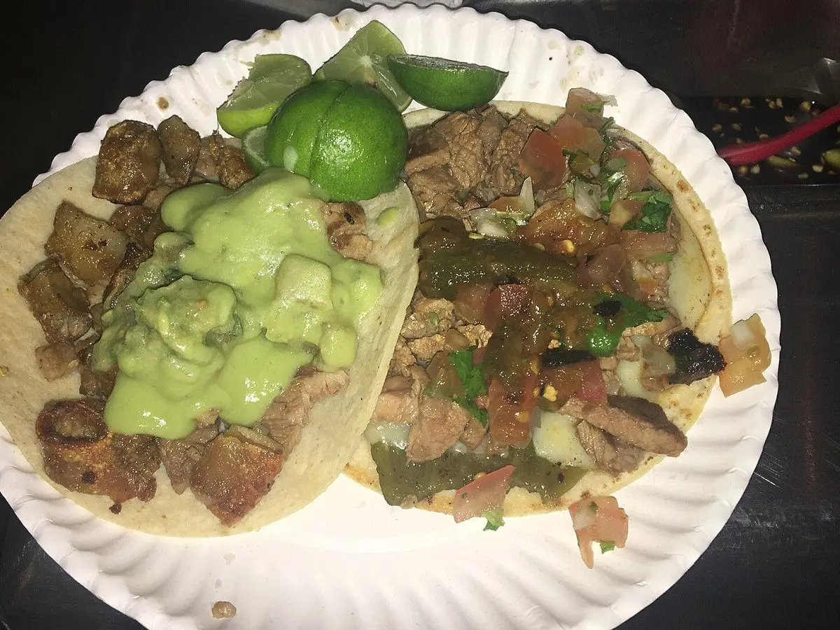Dos tacos de carne asada en tortilla de maíz con guacamole y una rodaja de lima en plato de papel