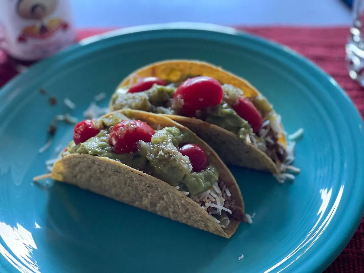 Tacos de tortilla crujiente rellenos de carne, tomate y guacamole sobre un plato azul