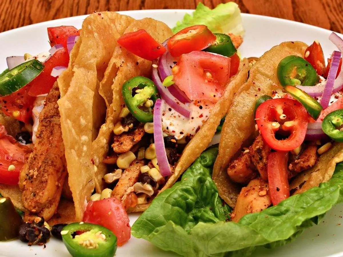 Tacos de pollo especiado con tomate, cebolla morada, maíz y jalapeño sobre hojas de lechuga