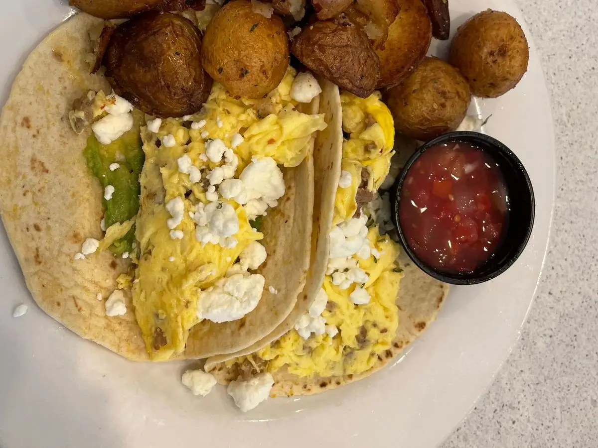 Tacos de desayuno con huevo revuelto y queso junto a patatas asadas y salsa roja