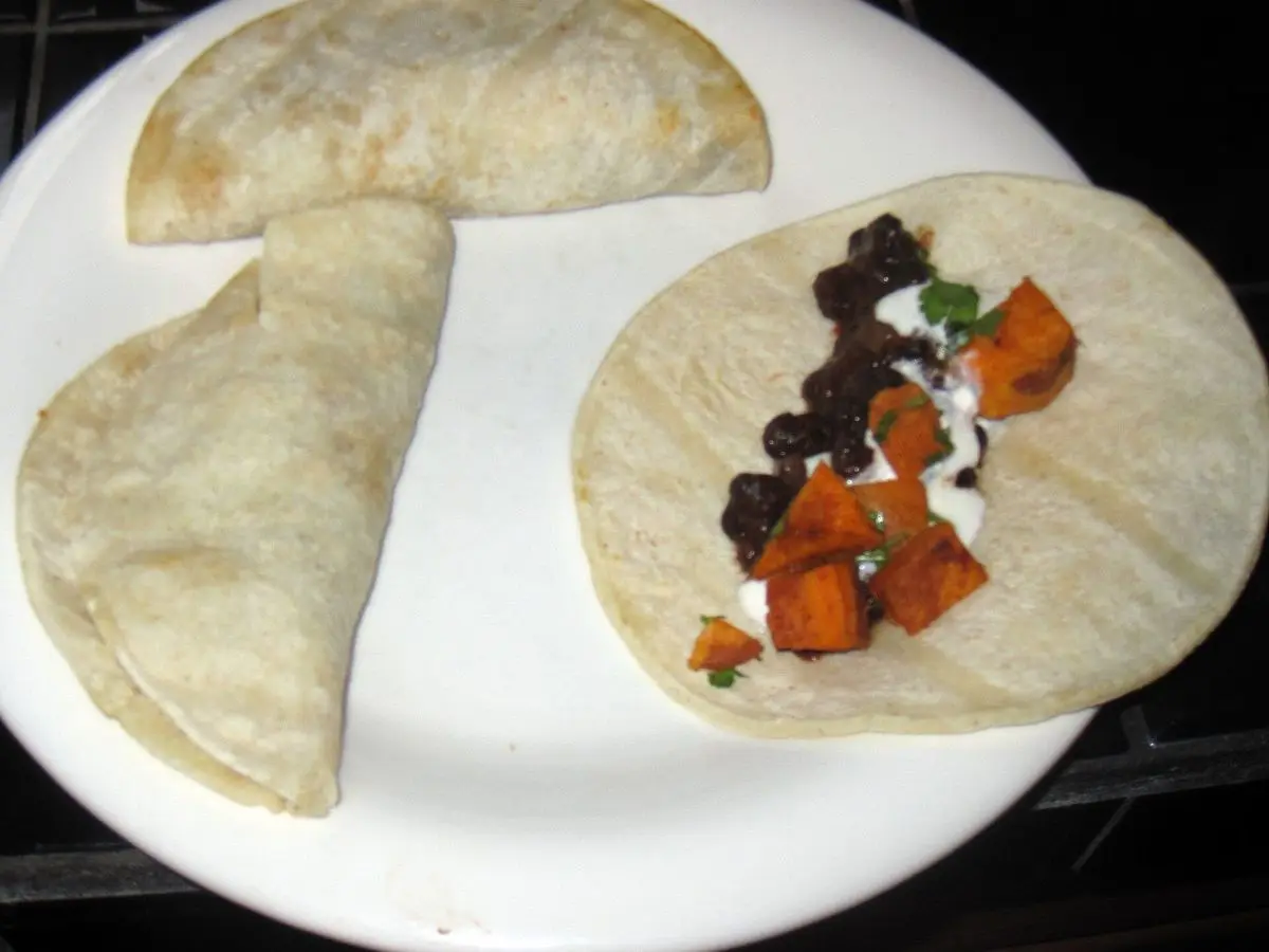 Taco de tortilla de maíz con frijoles negros, boniato asado y crema sobre un plato blanco