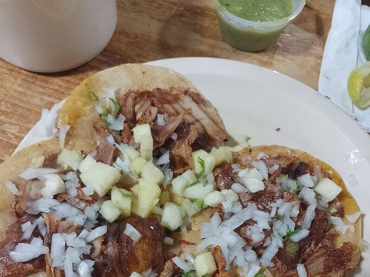 Tacos de carne de cerdo adobada con cebolla picada y trocitos de piña en un plato