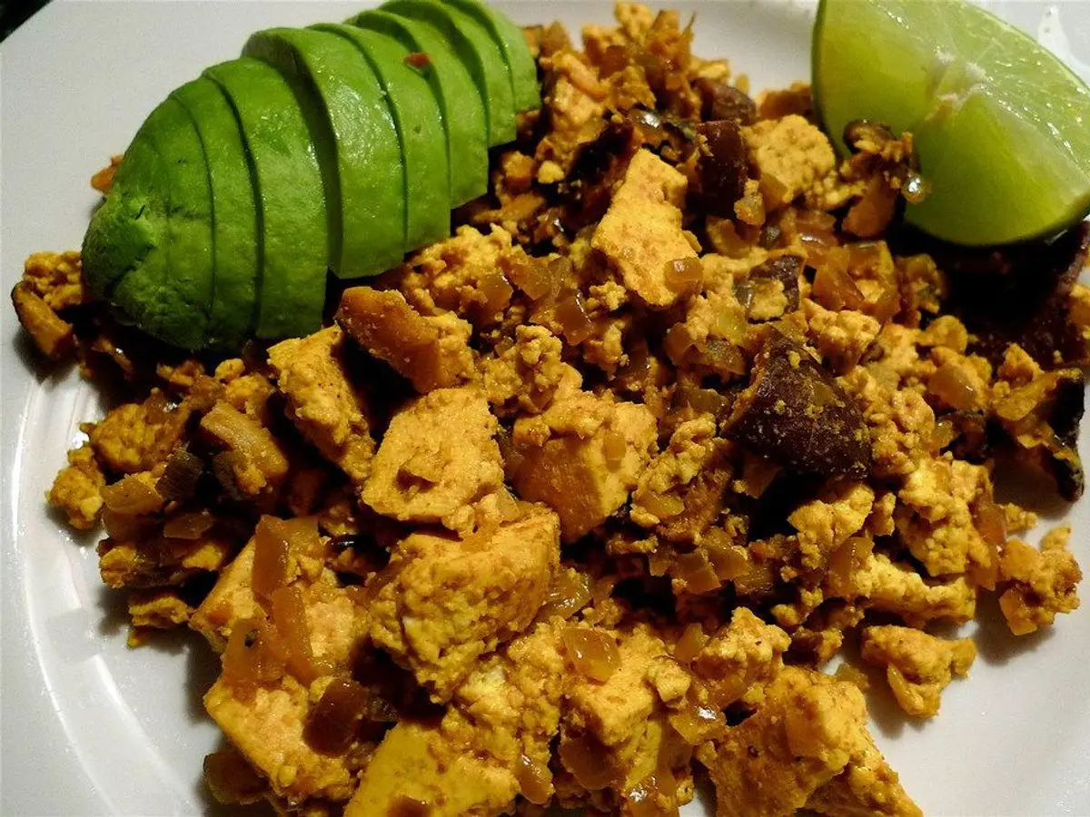 Plato de tofu revuelto especiado con aguacate en láminas y un gajo de lima