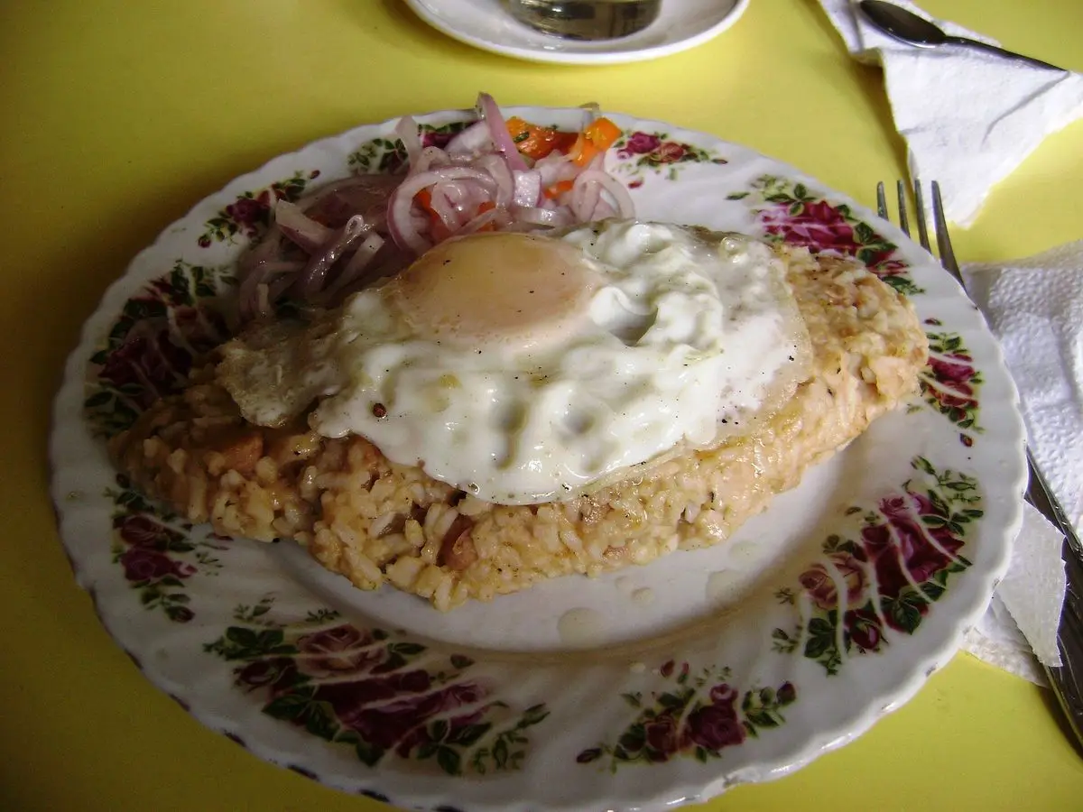 Tacu tacu de arroz y legumbres con huevo frito y cebolla morada en tiras sobre un plato decorado