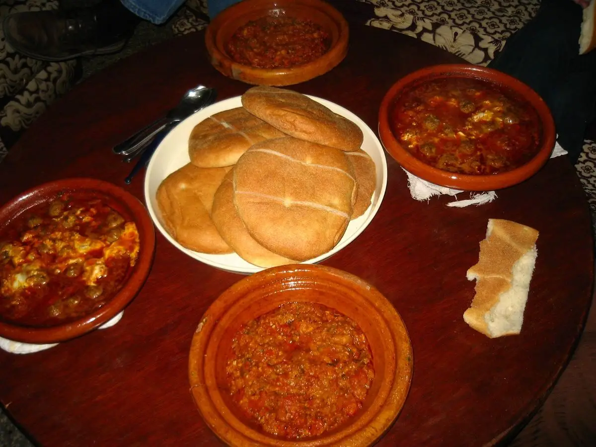 Cazuelitas de barro con albóndigas y salsa de tomate junto a pan plano marroquí sobre una mesa