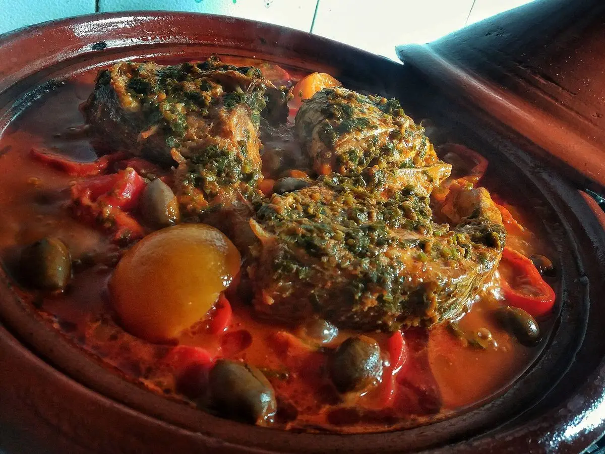 Tajín de pescado cubierto de chermoula de hierbas con pimientos rojos, aceitunas y limón en cazuela de barro