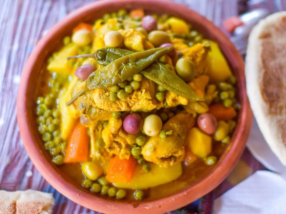 Tajín de carne con guisantes verdes, zanahoria, patata y aceitunas en una cazuela de barro