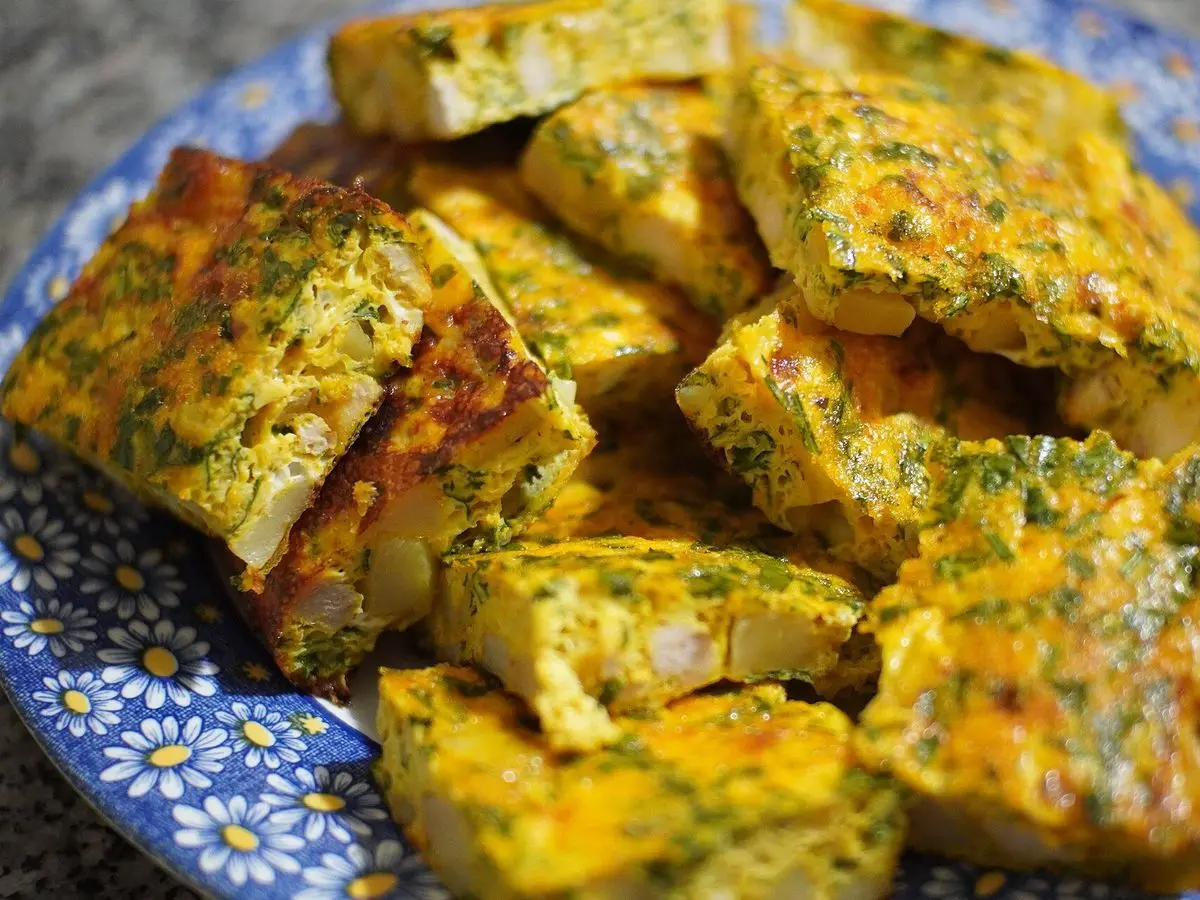 Plato decorado azul con porciones doradas de tajín tunecino al horno con huevo, queso y hierbas