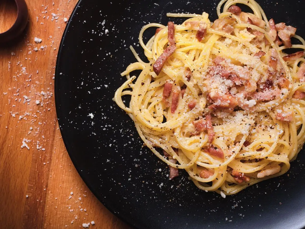 Espaguetis a la carbonara con queso rallado sobre un plato negro