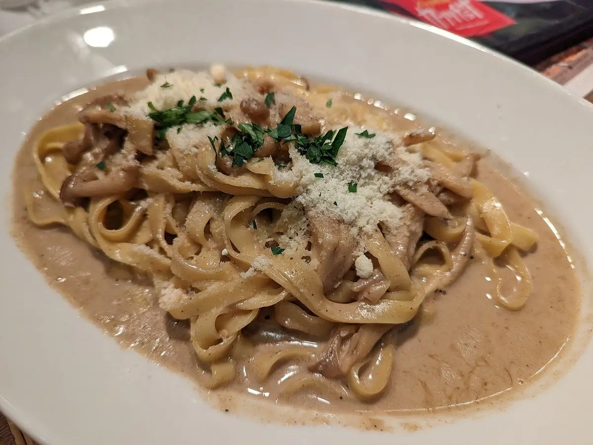 Tallarines en salsa cremosa de champiñones con queso rallado y hierbas en un plato hondo blanco