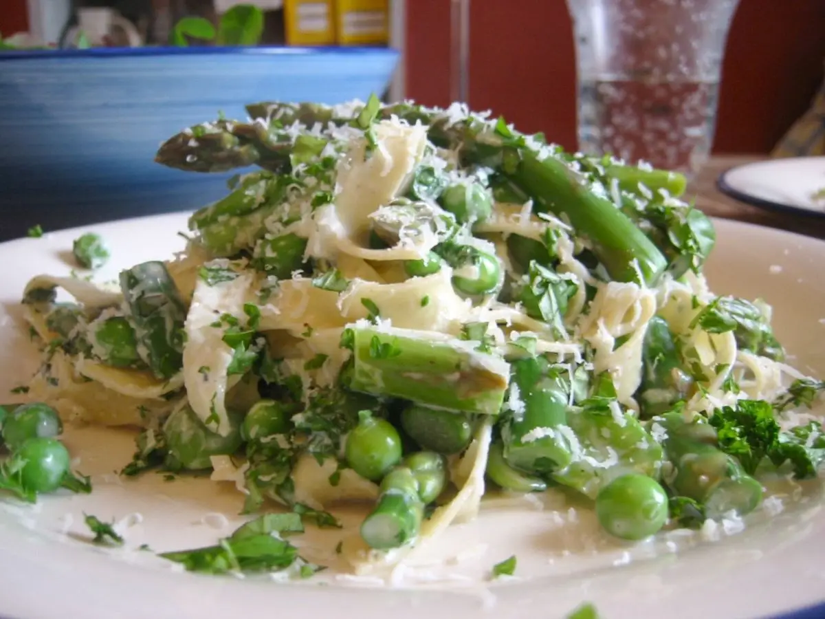Tallarines con espárragos verdes, guisantes y habas con hierbas frescas en un plato blanco