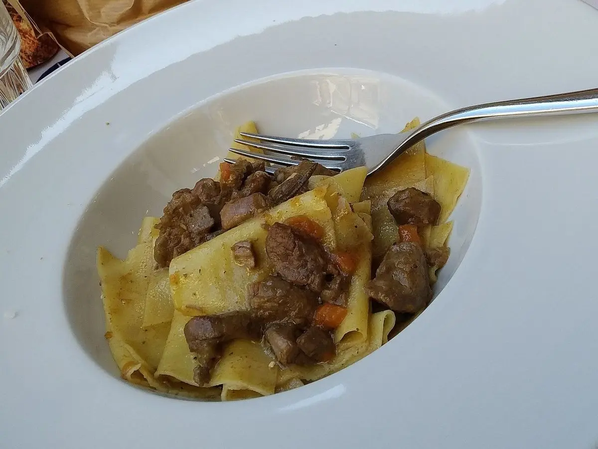 Plato hondo blanco con pasta fresca ancha al huevo y trozos de jabalí guisado, con un tenedor