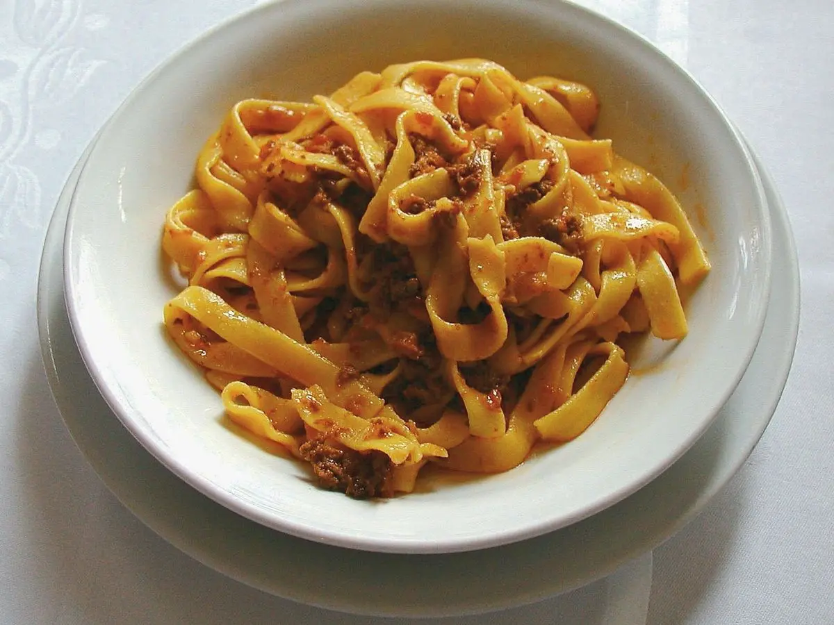 Cuenco blanco de tallarines con ragú de carne sobre un mantel blanco