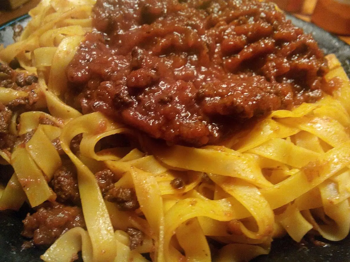Tallarines amarillos con una cucharada generosa de ragú de carne en salsa roja oscura